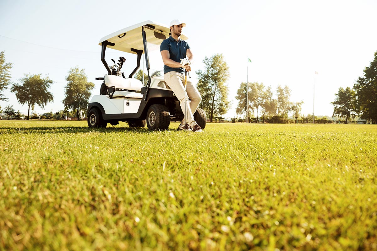 Young man resting while leaning on a golf cart and holding golf club