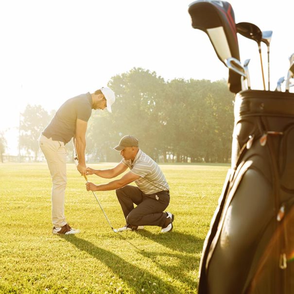 Personal trainer giving a lesson to a young male golfer while standing on a green course