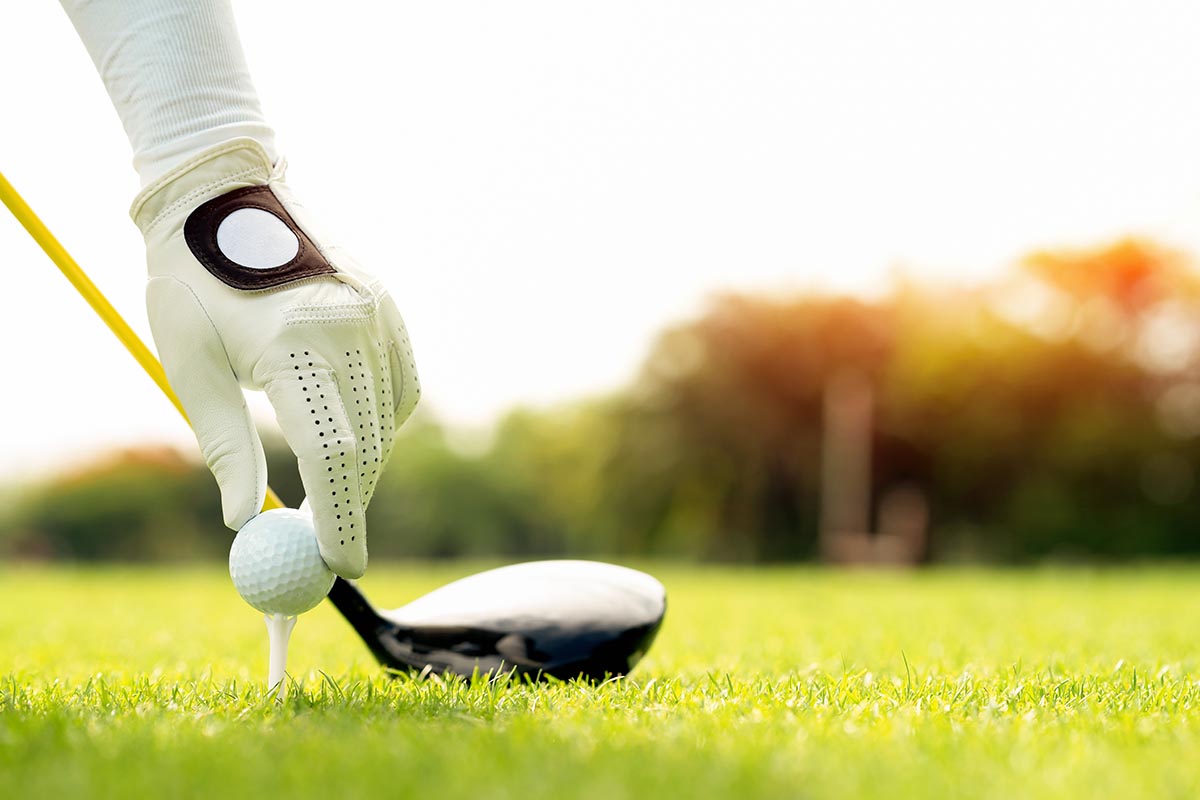 Golfer set the golf ball on the tee pin with club on course while on summer vacation. Hand holding golf ball with tee on course, tee off, copy space on Right side