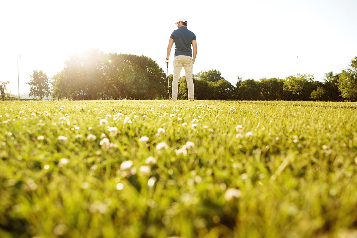 Back view of a male golf player at the green course with a golf club