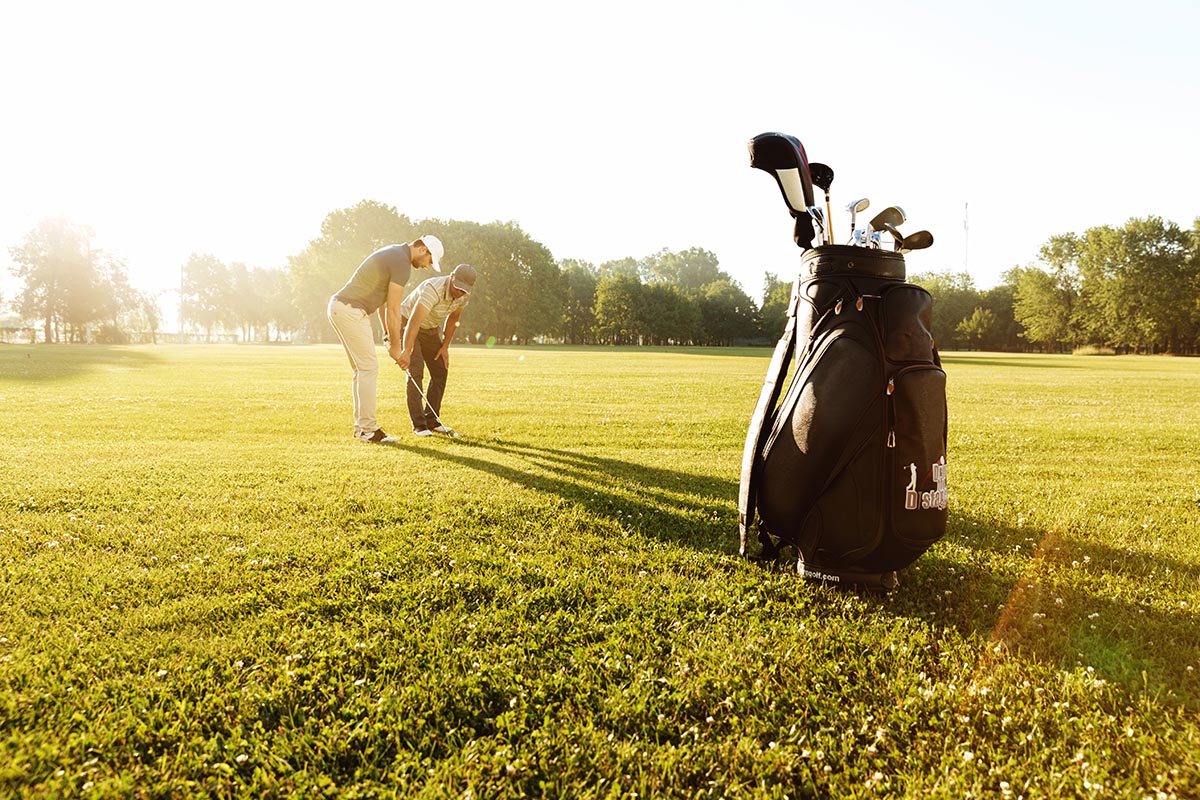 Senior male coach teaching young sportsman how to play golf at the green course